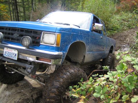 1990 Ford Bronco - This blue pickup truck, likely from the early 1990s, navigates a challenging off-road course with its large, aggressive tires.