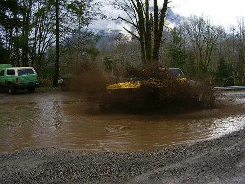 1990 Ford Bronco - A yellow 1990 Ford Bronco kicks up a massive spray as it drives through a deep mud puddle.