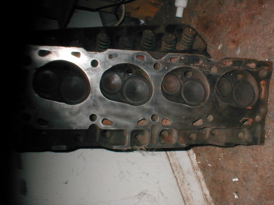 Cast-iron cylinder head deck face up on concrete showing four combustion chambers