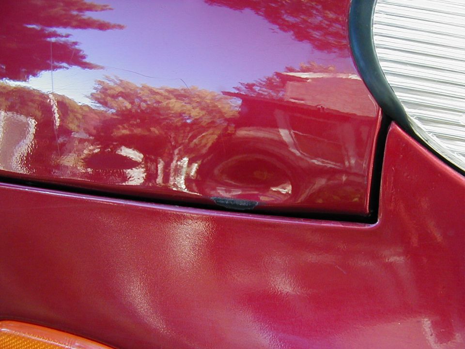 Close-up of a dent and paint chip on a maroon fender panel near the headlight of a red Ford Taurus