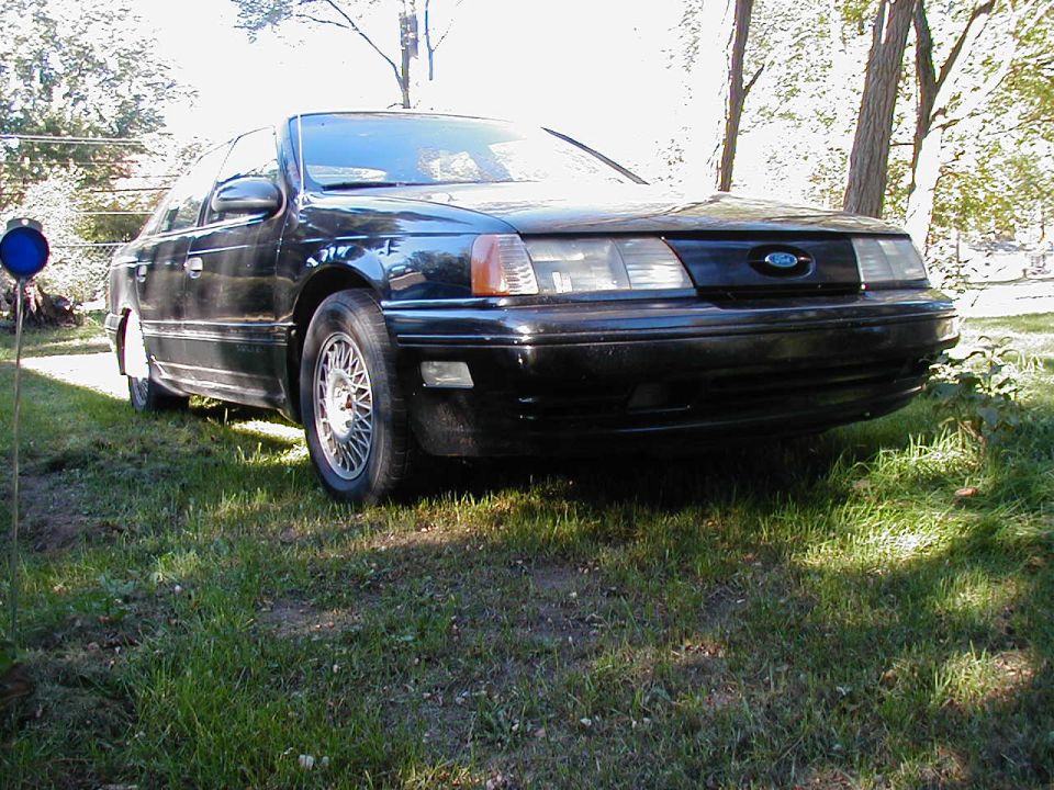 Black Ford Taurus sedan parked on grass, front three-quarter view with lace-style alloy wheels