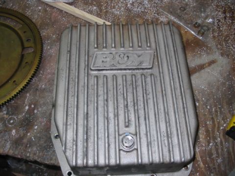 1997 Ford Crown Victoria - B&M finned aluminum transmission pan on a workbench next to a flywheel.