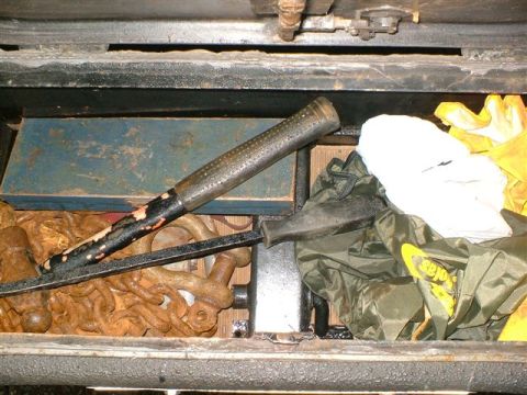 1989 Ford Bronco - Interior of a metal storage compartment, likely inside a bumper, containing rusty chain, shackles, a black-handled tool or pry bar, and stu…