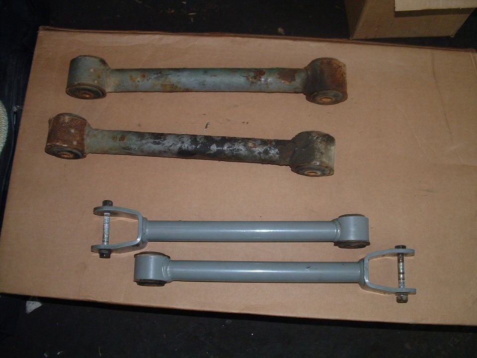 Two rusty control arms above two gray control arms with hardware