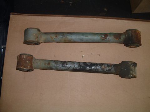 1994 Ford Bronco - Two aged suspension control arms lie on a flat surface, showing signs of wear and rust.