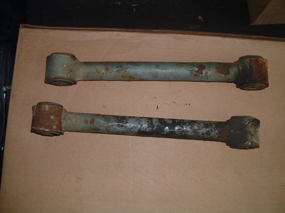 two rusty metal suspension control arms with rubber bushings