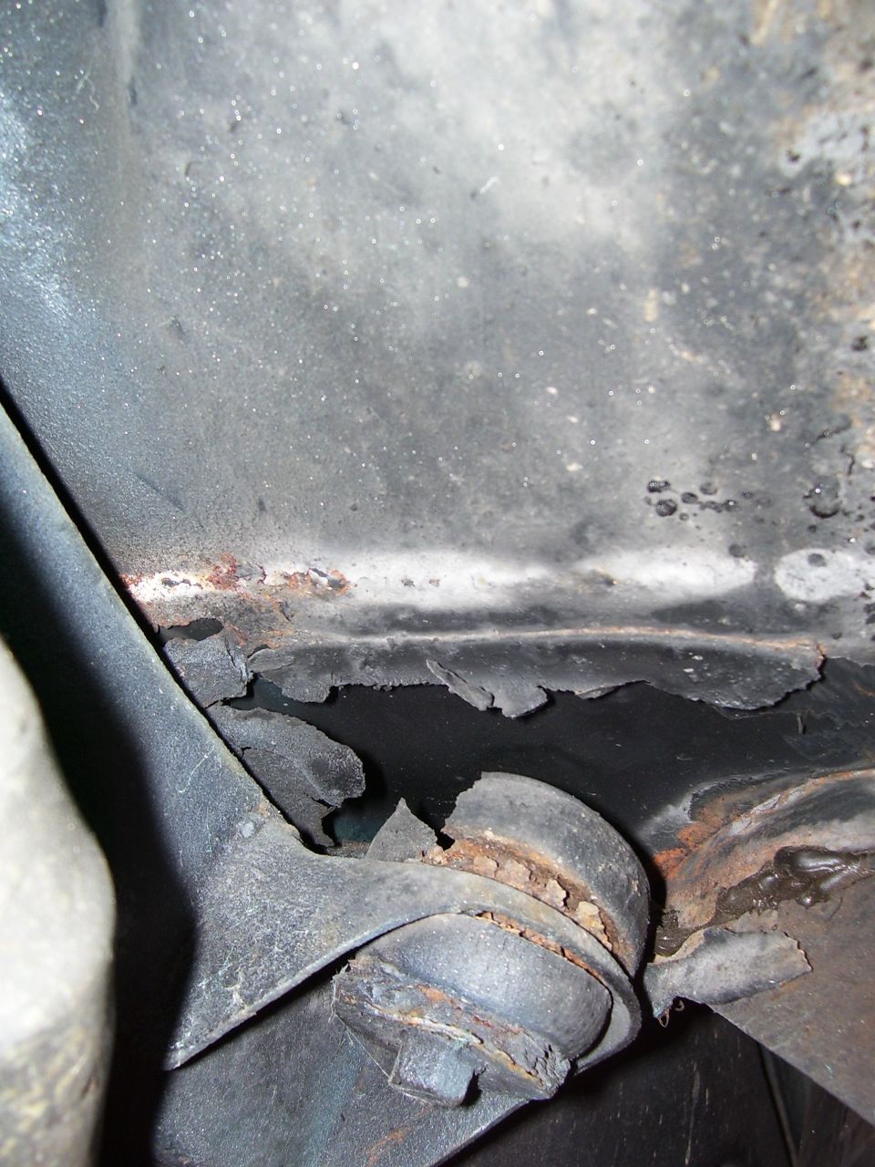 Rusty underbody seam and corroded bracket with peeling undercoating