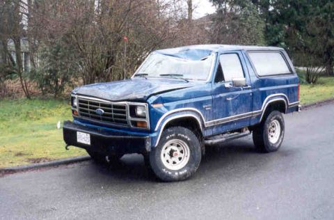 1989 Ford Bronco - This blue Ford Bronco has significant damage to its hood and windshield, suggesting it was involved in an accident.