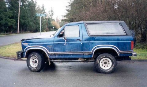 1989 Ford Bronco - This blue Ford Bronco is parked on a residential street with trees in the background.