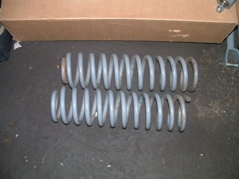 1994 Ford Bronco - Two gray coil springs are shown on a dark surface, with a cardboard box behind them.