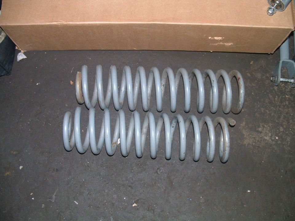 Two gray coil springs on a dark surface, with a cardboard box in the background