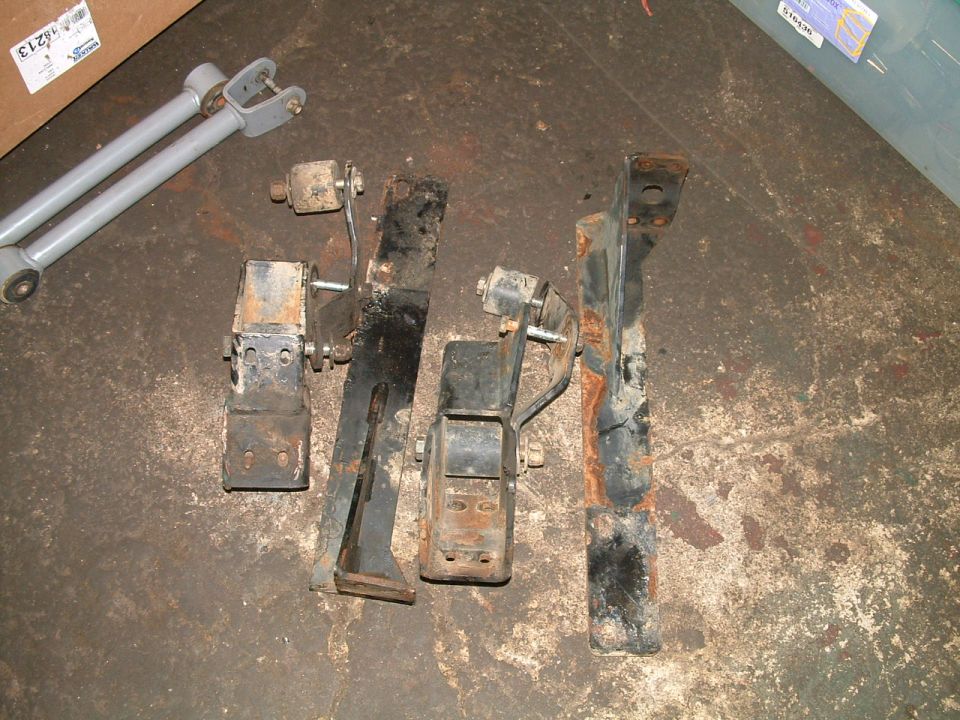 Several rusty metal suspension components and two gray control arms on a concrete floor