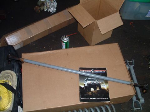 1994 Ford Bronco - A tie rod assembly lies on top of a large cardboard box next to an American Express 2004 performance off-road products catalog.