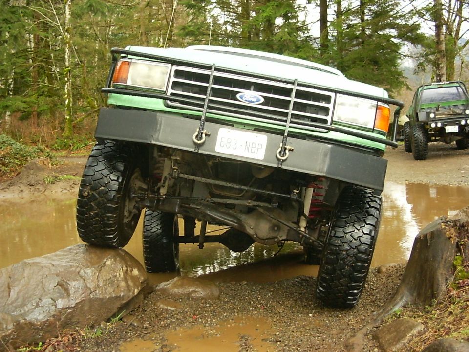 Green Ford Bronco off-roading, front view, tires on rocks and mud