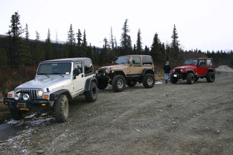 2003 Jeep TJ - Three Jeep Wranglers, including a silver 2003 TJ Rubicon, are parked on a gravel road in a wooded area.