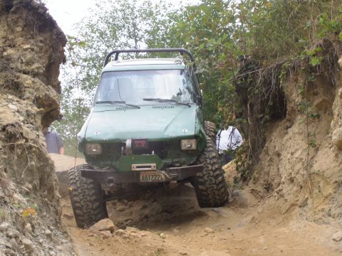 1990 Ford Bronco - Off-road vehicle navigating a challenging dirt path with steep embankments on either side.