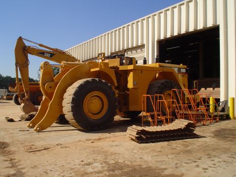 1966 International School Bus - A yellow Caterpillar wheel loader, model 990, is parked outside a building with its excavator arm extended.