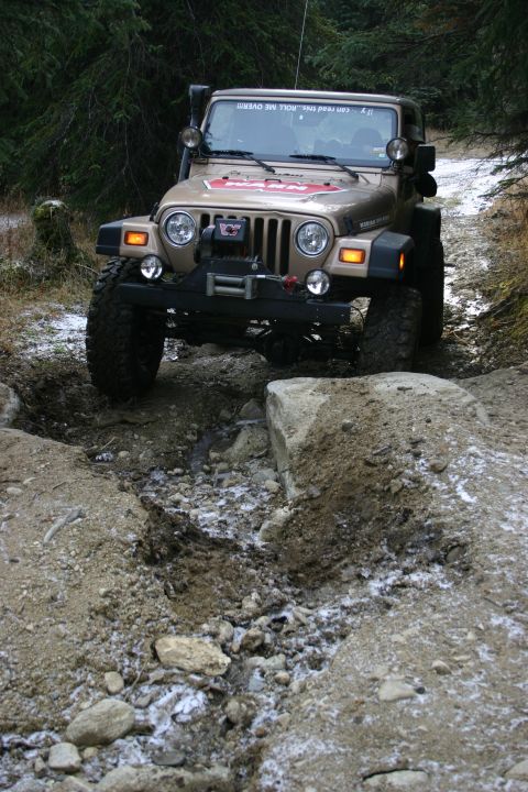 2003 Jeep TJ - A tan Jeep Wrangler TJ navigates a challenging rocky and snowy off-road path.
