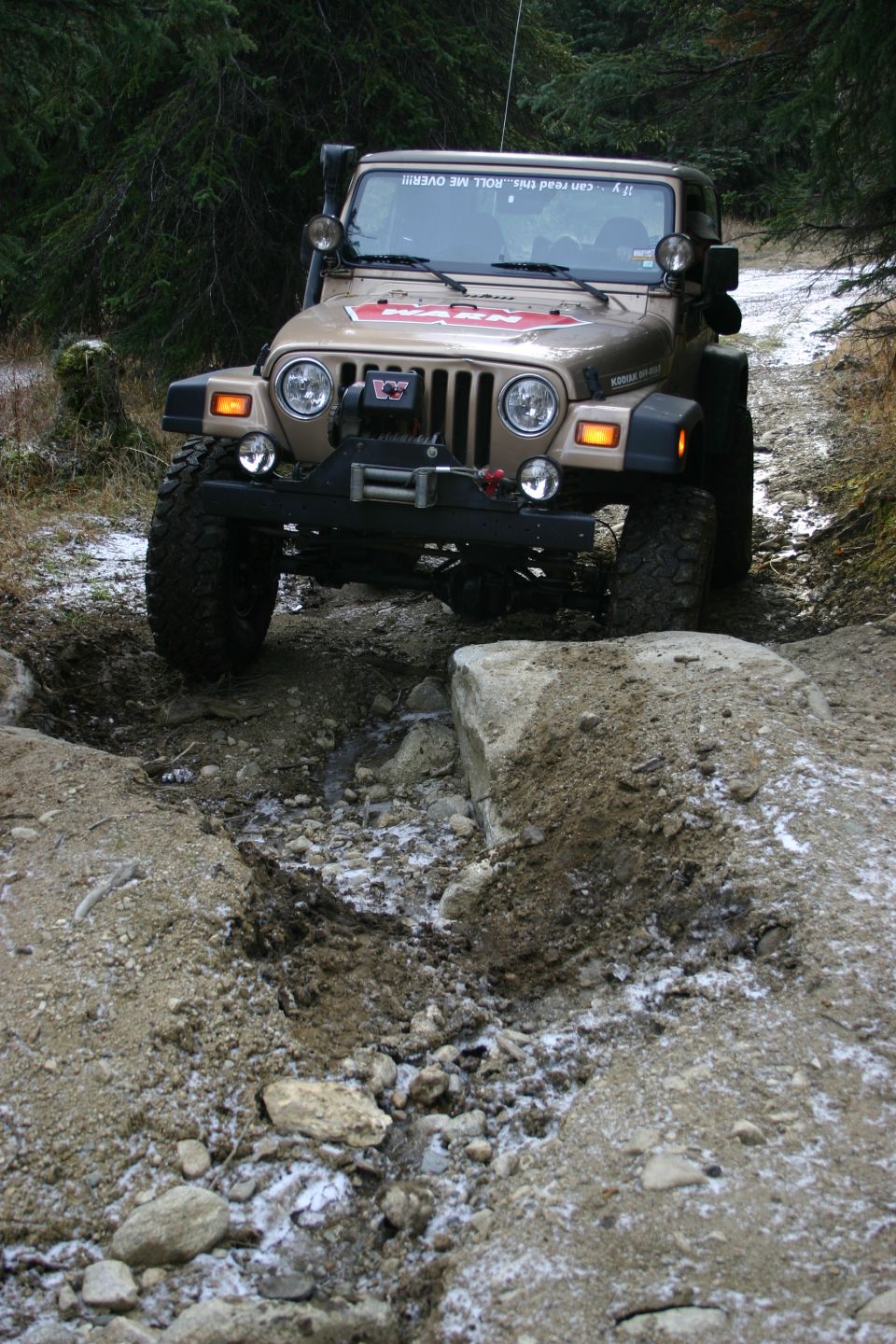 Tan Jeep Wrangler TJ with winch, off-roading on a rocky, snowy trail