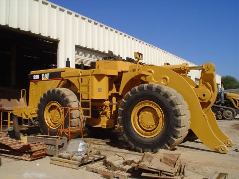 1966 International School Bus - A yellow Caterpillar 990 wheel loader is parked outside a building, with parts and tracks scattered around.
