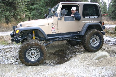 2003 Jeep TJ - A tan 2003 Jeep TJ navigates a challenging off-road course with large tires and lifted suspension.