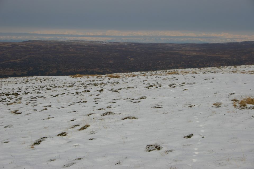 Snowy landscape with distant hills and a dark, overcast sky