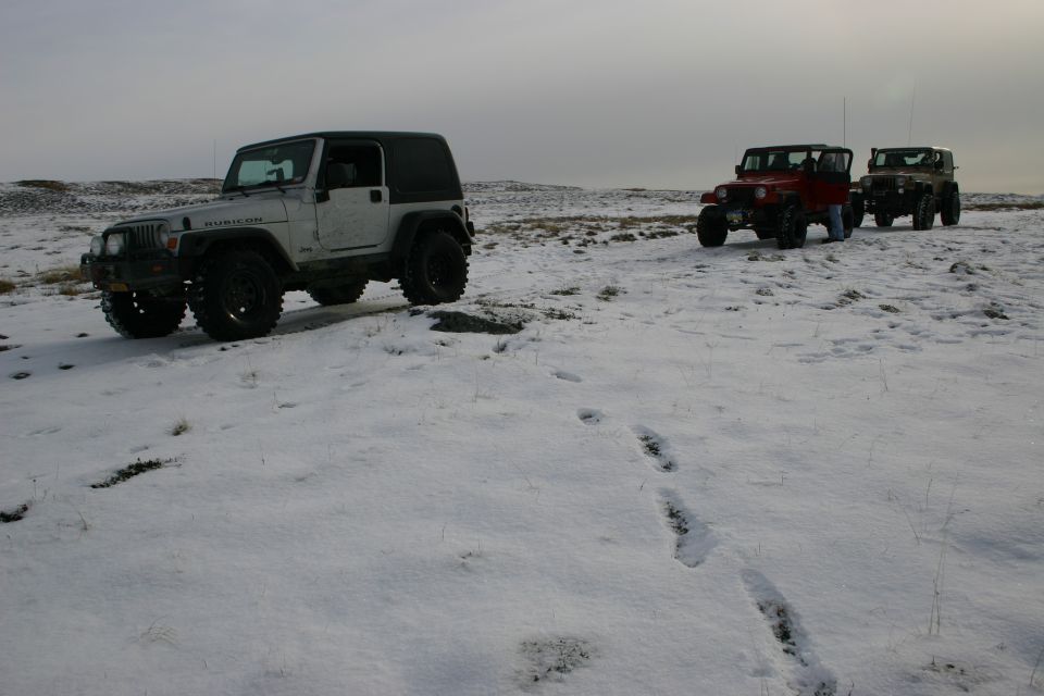 Silver Jeep Wrangler Rubicon with a black soft top parked in snow, front-left quarter view