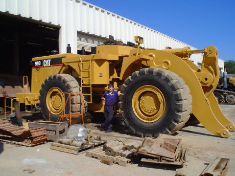 1966 International School Bus - A Caterpillar 990 wheel loader is shown with a worker standing next to its massive front tire.