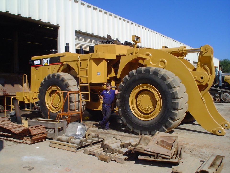 Yellow Caterpillar 990 wheel loader with a person standing by its front wheel