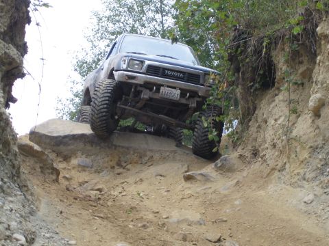 1990 Ford Bronco - This Toyota pickup truck is navigating a challenging off-road course with steep inclines and large rocks.
