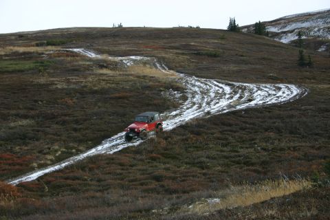 2003 Jeep TJ - Red 2003 Jeep TJ navigates a challenging muddy and snowy trail in an open, hilly landscape.