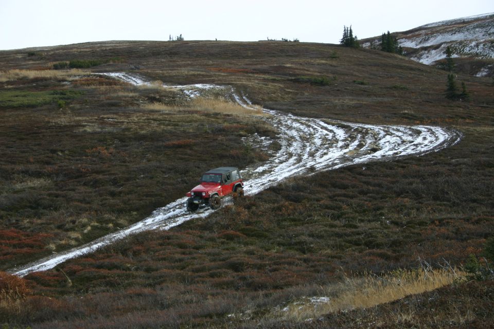 Red 2003 Jeep TJ driving on a muddy, snowy trail up a hill