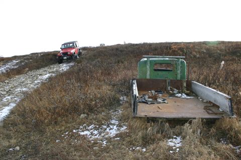 2003 Jeep TJ - A red Jeep Wrangler navigates a rocky incline, with a derelict green flatbed truck visible in the foreground.