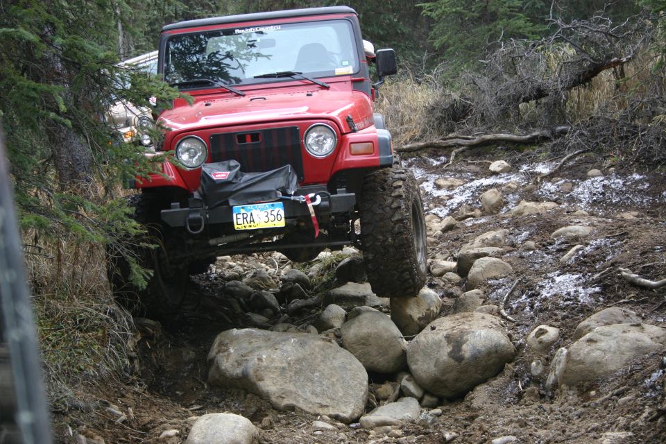 Red 2003 Jeep TJ navigating a rocky, wooded trail