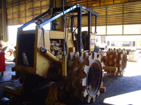 1966 International School Bus - A yellow compactor machine with spiked wheels is parked inside a garage, with other equipment visible in the background.