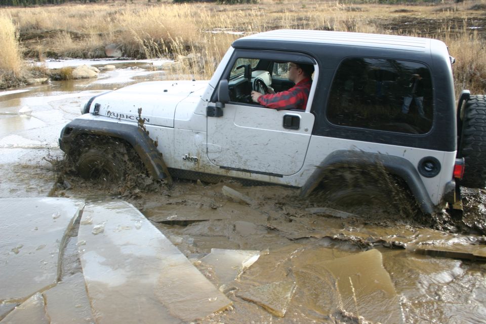 White 2003 Jeep TJ Rubicon stuck in mud and ice, driver visible inside