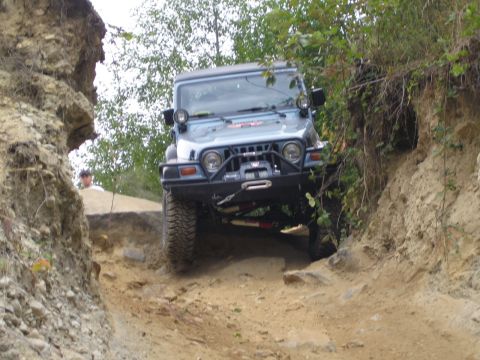 1990 Ford Bronco - This blue Jeep Wrangler is shown tackling a challenging off-road trail with steep inclines and rocky terrain.