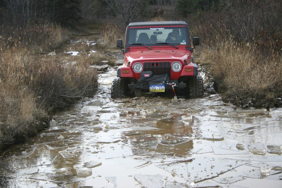 Red 2003 Jeep TJ driving through icy water on a dirt trail
