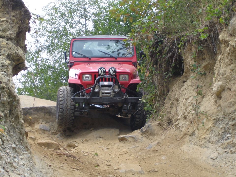 Red Jeep Wrangler driving on a dirt trail between rocky inclines