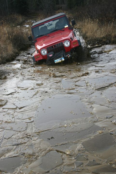 2003 Jeep TJ - A red 2003 Jeep Wrangler TJ navigates a challenging muddy and icy terrain.