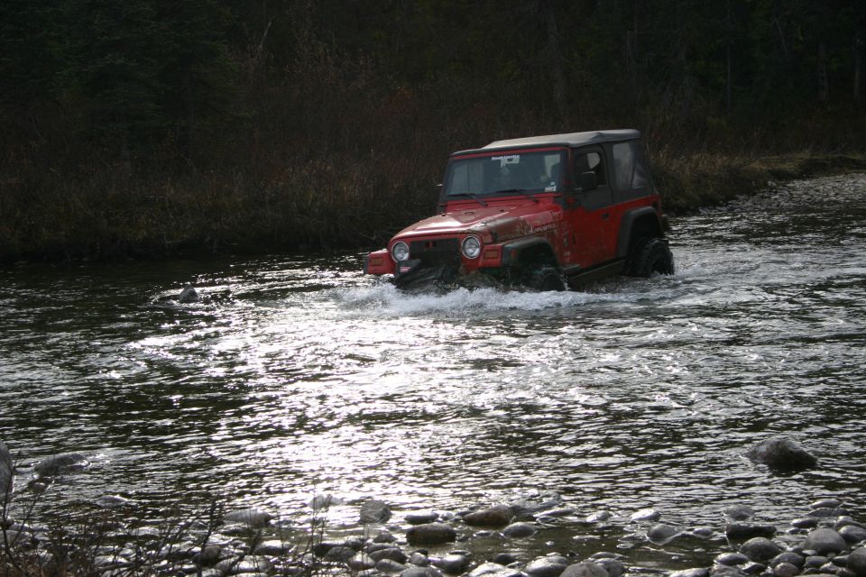 Red 2003 Jeep TJ driving through a rocky stream with water splashing