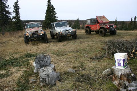 2003 Jeep TJ - Three Jeep TJs parked in a field; the red one has its hood open.