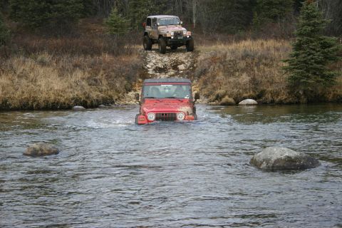 2003 Jeep TJ - A red Jeep Wrangler navigates a river while another Jeep waits on the bank.