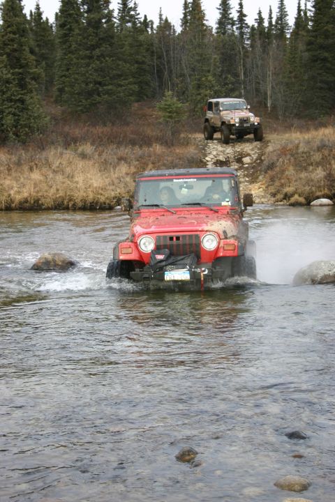 2003 Jeep TJ - A red 2003 Jeep TJ navigates a river crossing, with a second Jeep visible on the bank behind it.