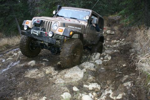2003 Jeep TJ - A tan 2003 Jeep Wrangler tackles a challenging rocky and muddy off-road path, demonstrating its off-road capabilities.