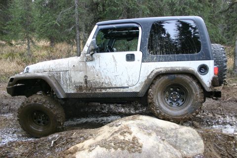 2003 Jeep TJ - 2003 Jeep TJ navigating a rocky, muddy trail in a wooded area.
