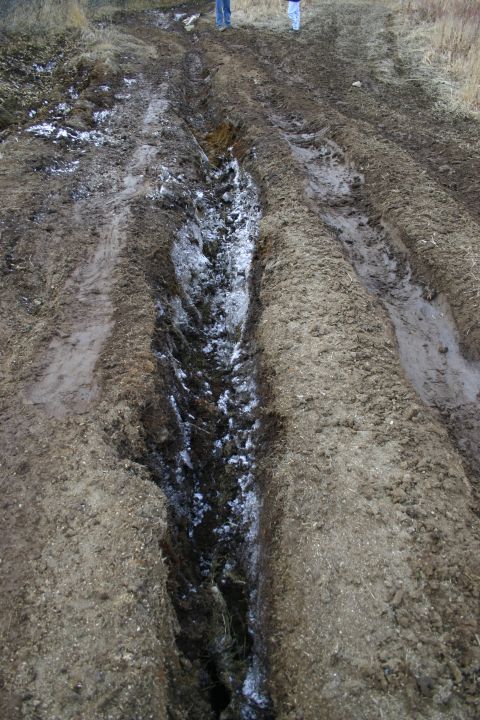 2003 Jeep TJ - A muddy track with snow and tire ruts, two people are visible in the background.