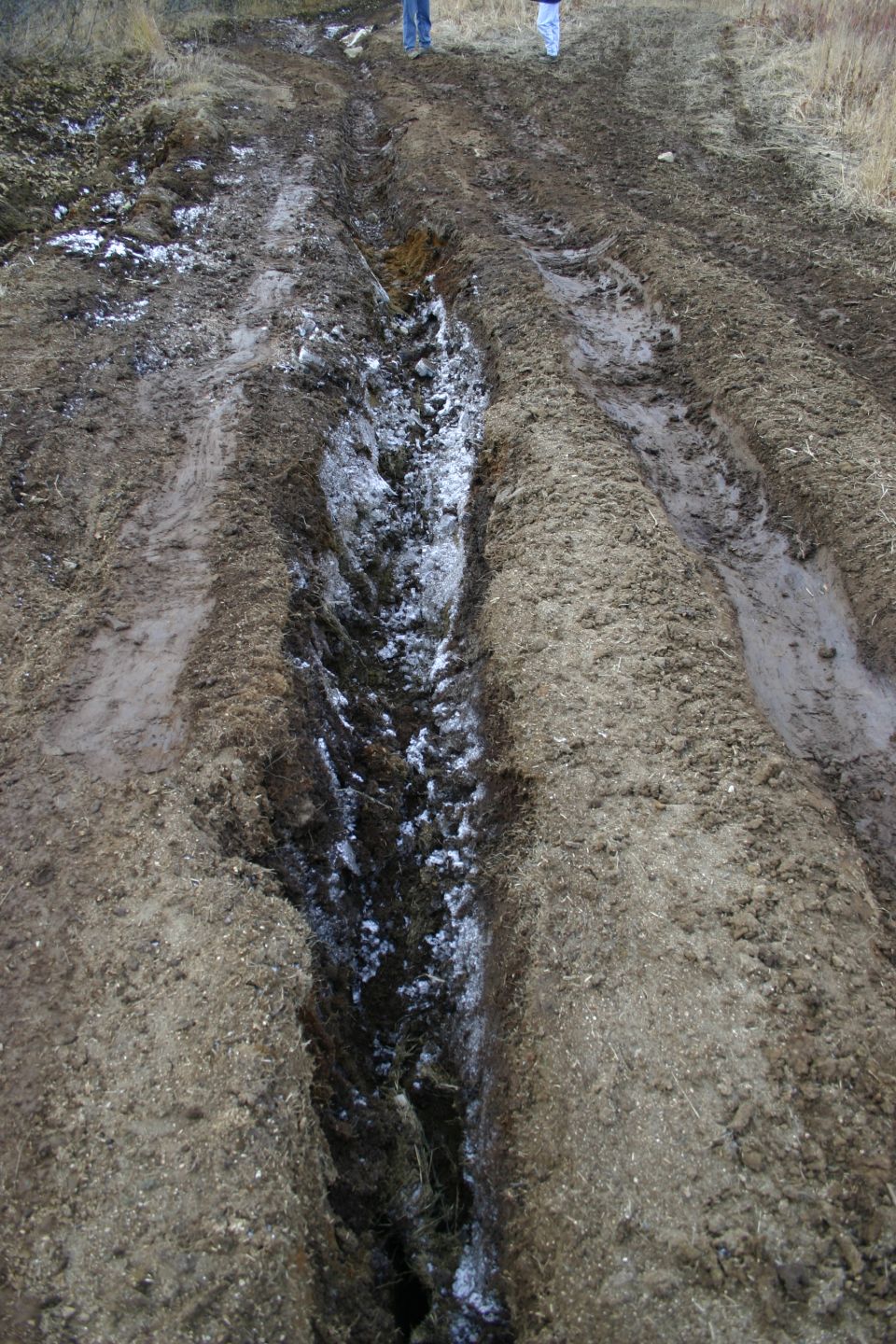 Muddy track with snow and tire ruts, two people standing in the distance