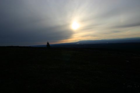 2003 Jeep TJ - A vast, dark landscape is illuminated by the sun breaking through clouds, with a lone tree visible on the horizon.