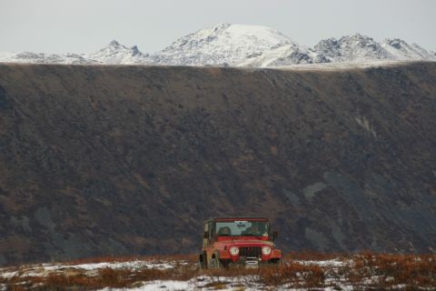 2003 Jeep TJ - A red Jeep TJ sits in a snowy, brush-filled field with a large, snow-capped mountain range behind it.